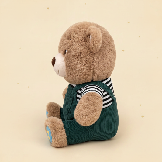 A Christian plush toy teddy bear sitting upright, wearing a dark green corduroy-style overalls outfit over a black-and-white striped shirt. The bear has light brown fur, a cream muzzle, and is photographed against a warm beige background decorated with faint golden stars.