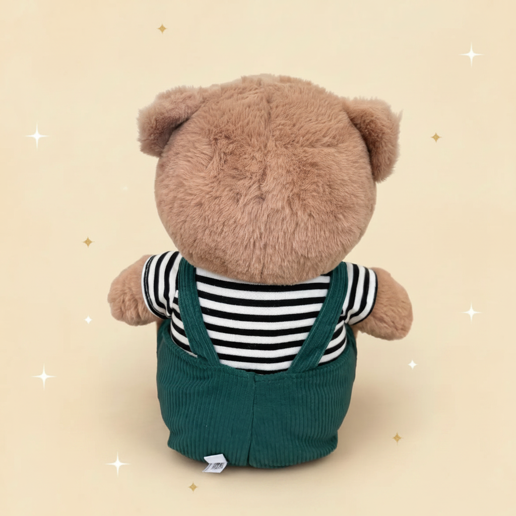 A Christian plush toy teddy bear toy shown from the back, wearing a black and white striped shirt and dark green corduroy overalls, set against a beige background with light brown  and white star illustrations.